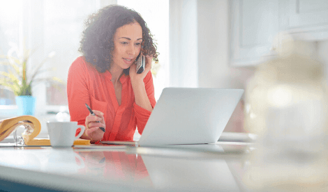 A smart woman working from home in front of laptop whilst holding a mobile phone to her ear - signifying getting support for the self-employed