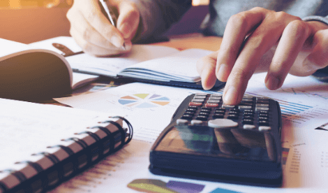 A man typing calculations into a calculator whilst adding notes into a notebook