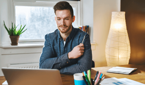 A smart casual looking man thinking in his home office in front of laptop screen