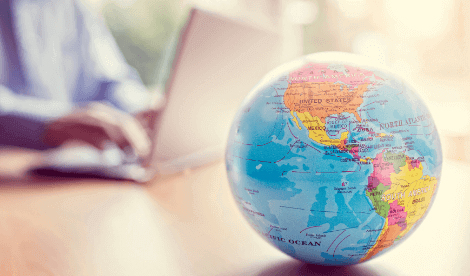 A globe in front of a man working in front of a laptop