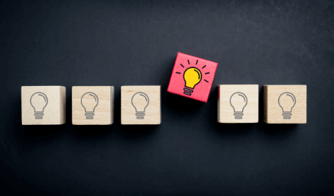 A number of wooden cubes with light bulbs, one in the middle is pink and placed above the rest to signal an idea