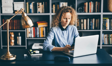 A woman working from home in library environment in front of laptop