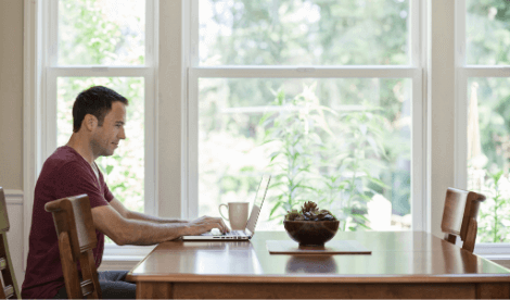 A happy man working from home on dining room table with laptop