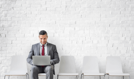 A smart business man in a waiting area sat next to empty chairs on his laptop