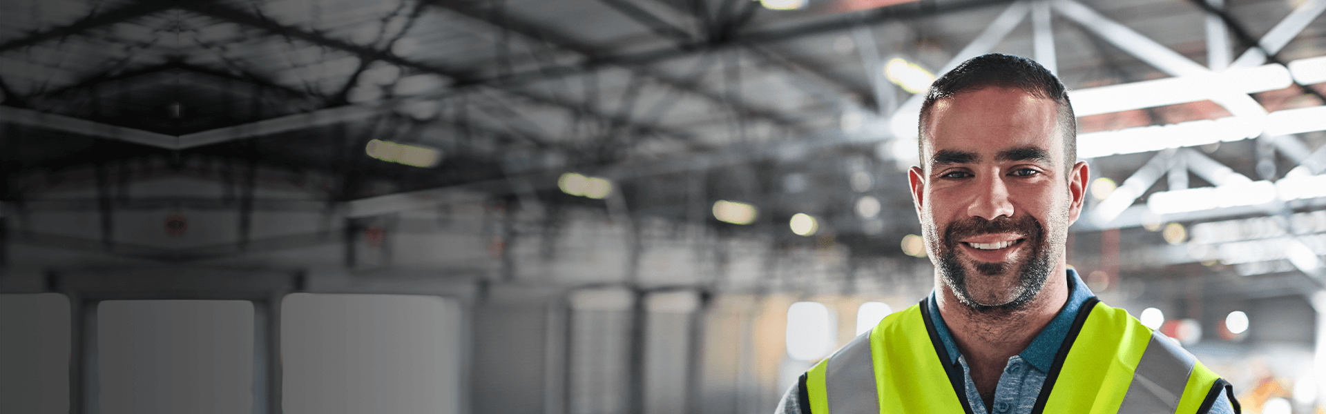 Man looking to camera in manufacturing setting, wearing a high visibility jacket.